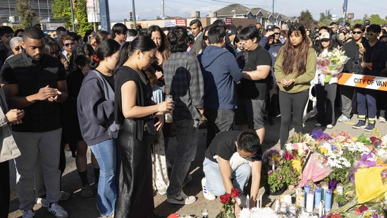 A group of mourners gathered at a memorial site in Vancouver, paying their respects after the tragic Lapu Lapu Day attack. People of diverse backgrounds, some with candles and flowers, stand in quiet reflection, honoring the victims. The somber gathering emphasizes the emotional toll the tragedy has taken on the community.